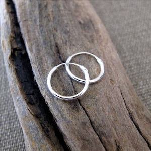 May include: Two silver hoop earrings on a wooden surface. The earrings are simple and classic, with a smooth finish.