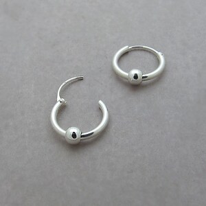 May include: A pair of silver hoop earrings with a small ball charm on each hoop.