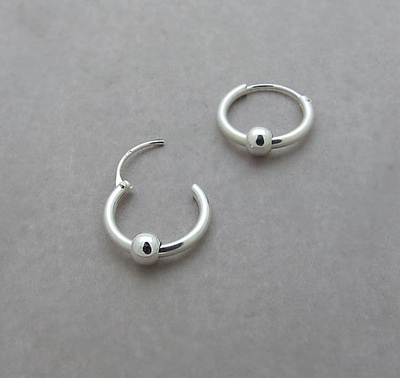 May include: A pair of silver hoop earrings with a small ball charm on each hoop.