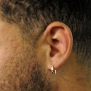 May include: A close-up of a person's ear with a silver hoop earring. The earring is simple and understated.
