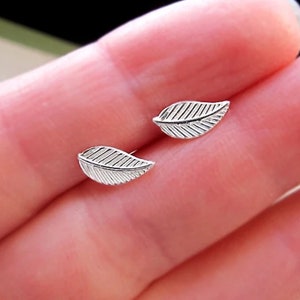 Puede incluir: Un par de pendientes de plata con forma de hoja. Los pendientes son pequeños y delicados, con un diseño sencillo.