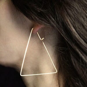 Op de afbeelding: Gouden driehoekige creolen. De oorbellen zijn groot en geometrisch.