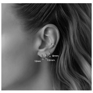 May include: Close-up of a person's ear with three different sized hoop earrings. The earrings are 8mm, 10mm, and 12mm in diameter.