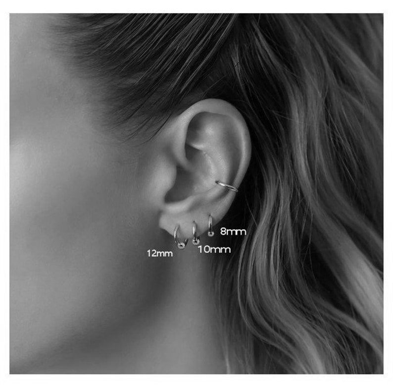 May include: Close-up of a person's ear with three different sized hoop earrings. The earrings are 8mm, 10mm, and 12mm in diameter.