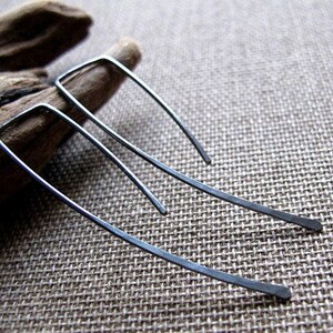 May include: A pair of silver earrings with a simple, geometric design. The earrings are made of thin, hammered metal and have a slightly curved shape.
