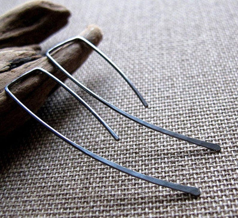 May include: A pair of silver earrings with a simple, geometric design. The earrings are made of thin, hammered metal and have a slightly curved shape.
