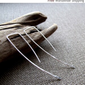 May include: A pair of silver earrings with a simple, minimalist design. The earrings are made of thin, curved wire and have a slightly angled shape.