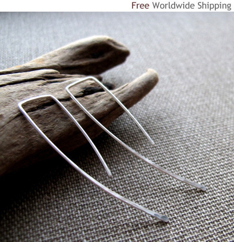 May include: A pair of silver earrings with a simple, minimalist design. The earrings are made of thin, curved wire and have a slightly angled shape.