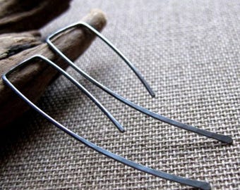 Può includere: Un paio di orecchini d'argento con un design semplice e minimalista. Gli orecchini sono realizzati in metallo sottile e curvo e hanno una forma rettangolare.