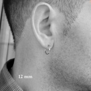 May include: A silver hoop earring with a 12 mm diameter. The earring is worn in the left ear of a person.