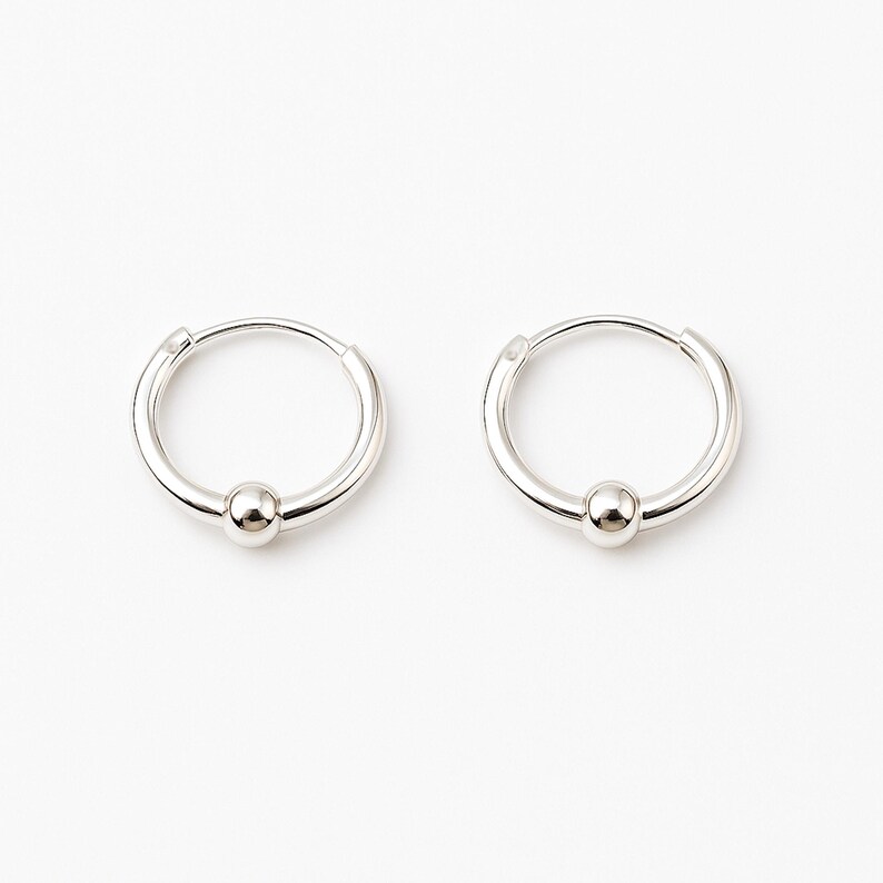 Two silver hoop earrings with a small silver ball at the bottom of each hoop.