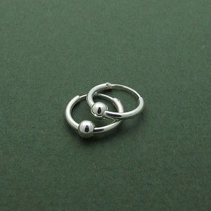 May include: A pair of silver hoop earrings with ball closures. The earrings are small and delicate.