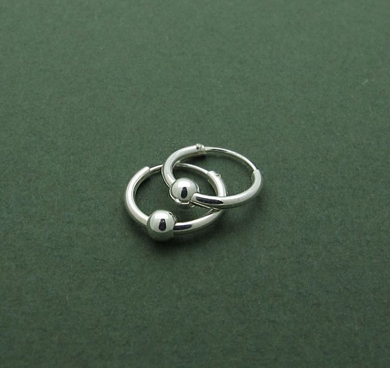 May include: A pair of silver hoop earrings with ball closures. The earrings are small and delicate.