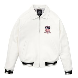 Peut inclure: Veste de bombardier blanche avec col et fermeture &eacute;clair. Le blouson pr&eacute;sente des poignets et un ourlet ray&eacute;s noirs et blancs. Un &eacute;cusson brod&eacute; avec le texte "AVIREX" et un motif de drapeau am&eacute;ricain est sur la poitrine.