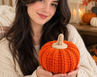 Puede incluir: Una calabaza redonda tejida a ganchillo en un color naranja vibrante, con una superficie texturizada y acanalada y un pequeño tallo de color beige claro unido al centro superior. La calabaza está hecha de hilo con puntadas visibles.