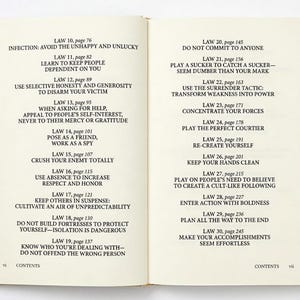 May include: Open book with text on the pages. The left page lists laws with page numbers, such as "Law 10, page 76: Infection: Avoid the Unhappy and Unlucky." The right page continues with more laws.
