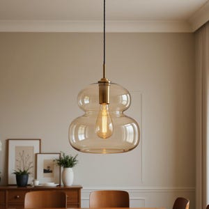 May include: A pendant light featuring a double-gourd shaped, amber-tinted glass shade suspended by a black cord. The fixture includes a brass-toned metal socket and a single exposed filament light bulb centered within the glass structure.