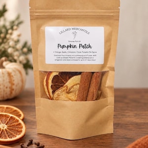 May include: A brown paper pouch containing a simmer pot kit labeled Lillard Mercantile Pumpkin Patch. The clear window reveals dried orange slices, apple slices, and cinnamon sticks. The label lists ingredients including orange, apple, cinnamon, clove, and pumpkin pie spice.