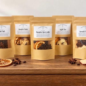 May include: Five brown paper stand-up pouches labeled Lillard Mercantile with scents Cozy Cafe, Pumpkin Patch, Pumpkin Spice Latte, Apple Pie, and Sweater Weather. Each pouch has a clear window showing dried fruit, coffee beans, and spices.