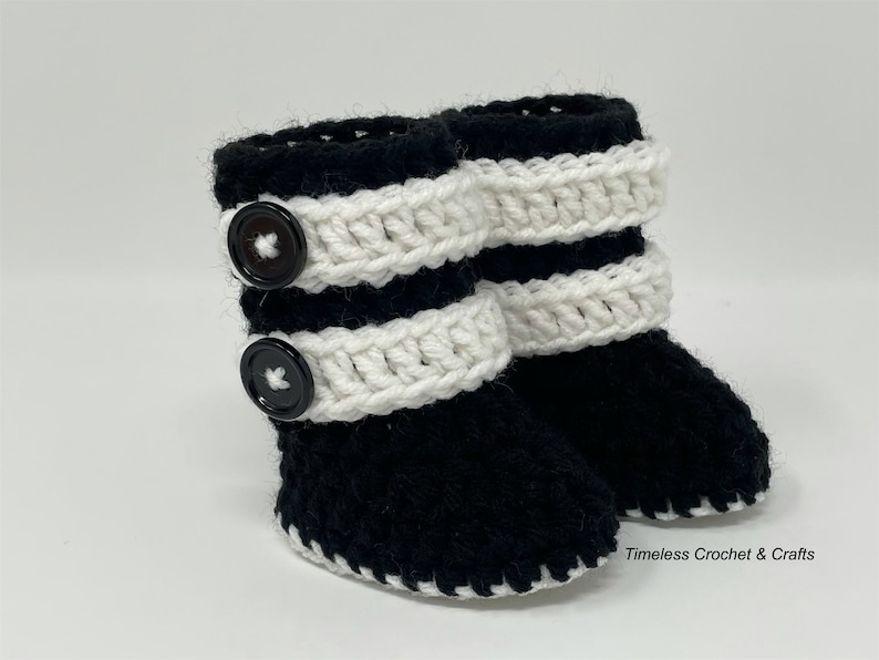 May include: Black and white crocheted baby booties with black buttons. The booties have a white crocheted trim around the top and bottom.