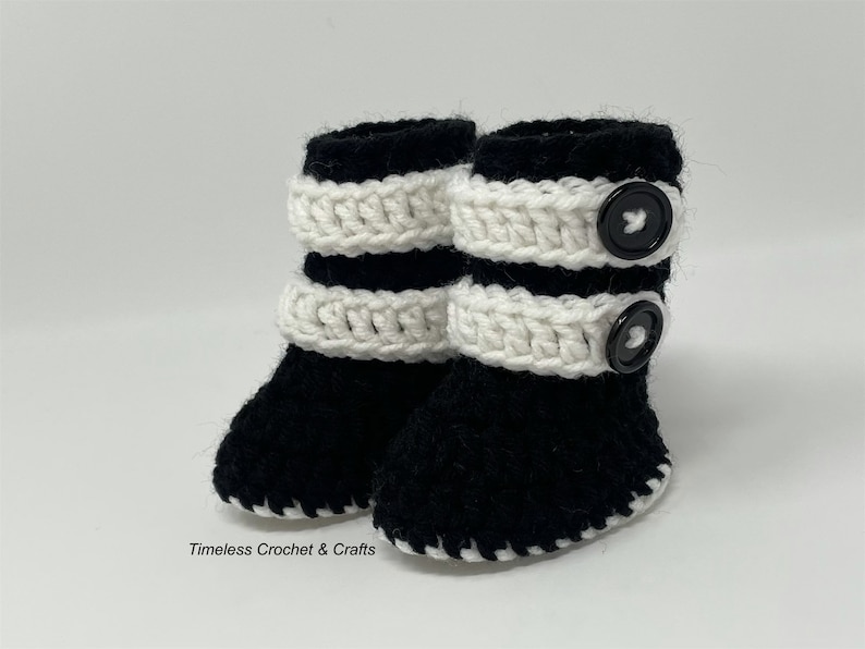 May include: A pair of black and white crocheted baby booties with black buttons. The booties have a white crocheted band around the top and a black crocheted sole.
