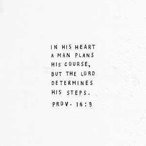 May include: A white background with black text that reads "IN HIS HEART A MAN PLANS HIS COURSE, BUT THE LORD DETERMINES HIS STEPS. PROV. 16:9"