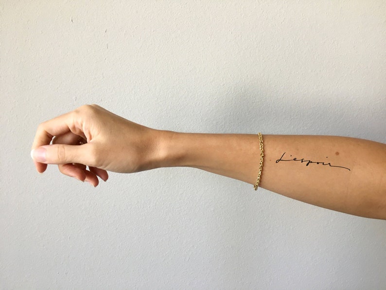 May include: A person's arm with a temporary tattoo that says "Liebspin" in cursive script.