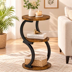 May include: A three-tier side table featuring a black metal S-shaped frame and three round, wood-grain shelves. The top shelf holds a white vase and a candle, the middle shelf holds two books and a gold bird figurine, and the bottom shelf holds a woven basket.