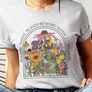 May include: A gray t-shirt with a floral graphic and the text "Restore Native Plants - Restore Native Ecosystems".
