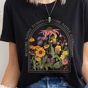 Black tee saying restore native plants. Image of a coneflower surrounded by many other wildflowers