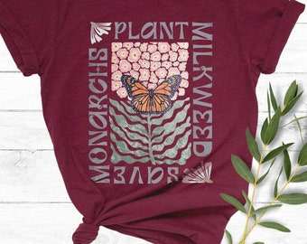 Könnte beinhalten: Ein maroonfarbenes T-Shirt mit einem grafischen Design, das einen Schmetterling, Blumen und den Text "Pflanze Seidenpflanzen, rette die Monarchfalter" zeigt.