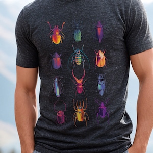Peut inclure: Un t-shirt gris foncé chiné avec un motif d'insectes colorés. Les insectes sont disposés en grille et sont de formes et de tailles différentes.