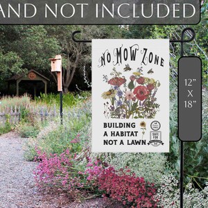 K&ouml;nnte beinhalten: Eine Gartenflagge mit dem Text "NO MOW ZONE" und einem floralen Design. Die Flagge misst 30 cm x 46 cm und tr&auml;gt den Schriftzug "BUILDING A HABITAT NOT A LAWN". Die Flagge wird in einem Garten gezeigt.