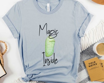May include: A light blue t-shirt with a green and white butterfly chrysalis graphic and the text "Magic Inside".