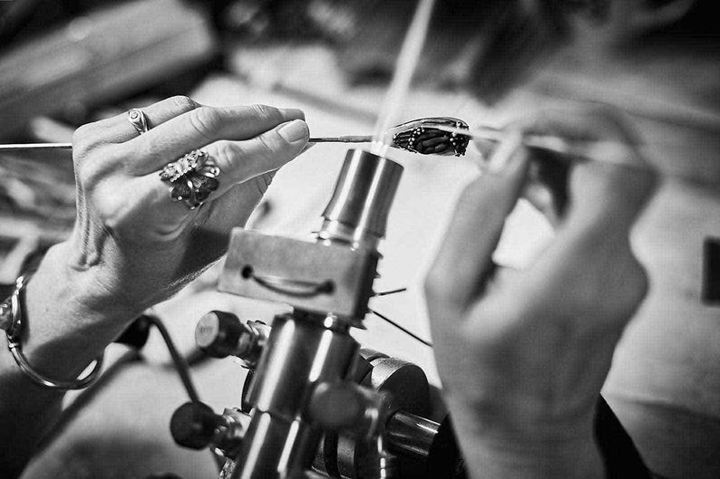 Artist Jude Rose makes a glass bead in the flame of her torch. Two hands working, holding a steel mandrel and glass rod. www.juderose.com