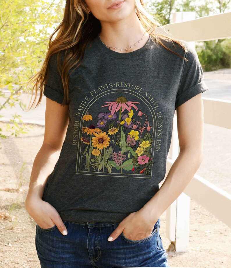 K&ouml;nnte beinhalten: Ein dunkel-helles graues T-Shirt mit einer Grafik einer Vintage-botanischen Illustration von Blumen in einem Fensterrahmen. Der Text um den Rahmen lautet "Restore Native Plants Restore Native Ecosystems".