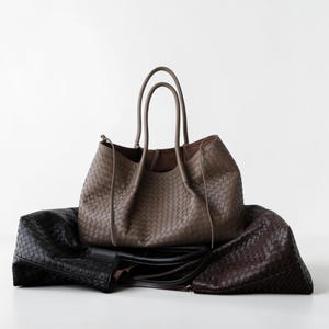Könnte beinhalten: Eine Kollektion aus drei geflochtenen Ledertaschen in Taupe, Schwarz und Dunkelbraun. Jede Tasche zeichnet sich durch ein markantes Flechtmuster, zwei Tragegriffe und ein geräumiges, offenes Design mit einer weichen, flexiblen Struktur aus.