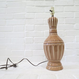May include: A brown ceramic table lamp with a white stripe design. The lamp has a cord and plug.