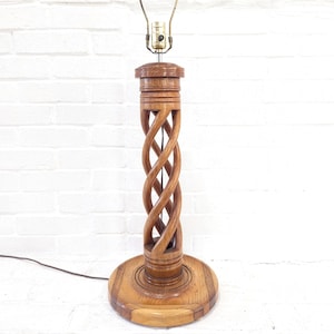 Könnte beinhalten: Holz-Tischlampe mit einem einzigartigen, gedrehten Design an der Mittelsäule. Die Lampe hat einen runden Sockel und eine Lampenfassung aus Messing. Das Holz hat eine warme, natürliche Oberfläche. Die Lampe ist eingesteckt.