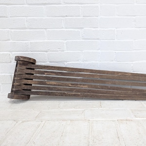 May include: A rustic wooden bench with a slatted design. The bench is made of dark brown wood and has a unique, angled shape. The bench is approximately 122 cm long.