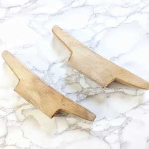 May include: Two wooden shoe forms, also known as shoe trees, are shown on a white marble surface. The shoe forms are light brown in color and have a slightly curved shape.