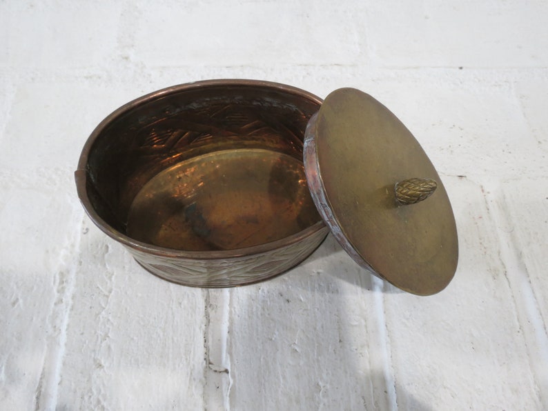 Op de afbeelding: Een ovale messing doos met een deksel. De doos heeft een reli&euml;fmotief en een kleine knop op het deksel.