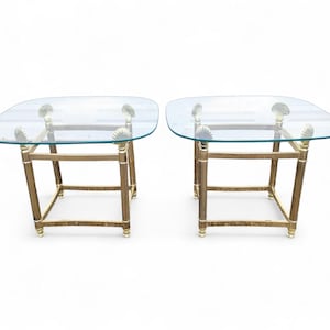 May include: Two square glass-top side tables with brass-colored metal frames. Each table has four seashell accents supporting the glass. The tables have a vintage, coastal design.