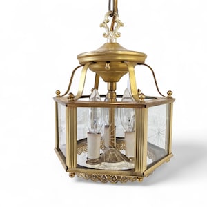 May include: A gold-toned brass chandelier with a hexagonal glass shade. The shade has a decorative etched pattern and features four light bulbs.