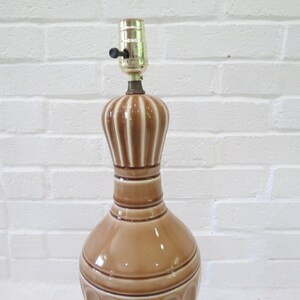 May include: A brown ceramic table lamp with a white stripe design. The lamp has a simple, classic design and would look great in a variety of home decor styles.