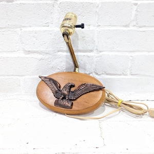 Puede incluir: Una lámpara de pared de madera con un diseño de águila de latón y un cable con un enchufe. La lámpara tiene un casquillo para bombilla y un cable con un enchufe.