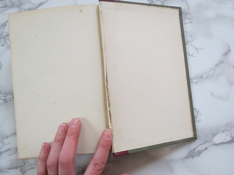 K&ouml;nnte beinhalten: Ein ge&ouml;ffnetes Buch mit gr&uuml;nem Einband und wei&szlig;en Seiten. Das Buch liegt flach auf einer wei&szlig;en Marmorfl&auml;che.