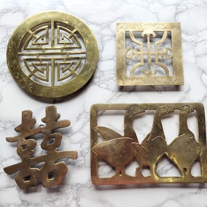 May include: Four brass decorative objects. A round piece with a geometric design, a square piece with an ornate pattern, a double happiness symbol, and a rectangular piece with three geese.