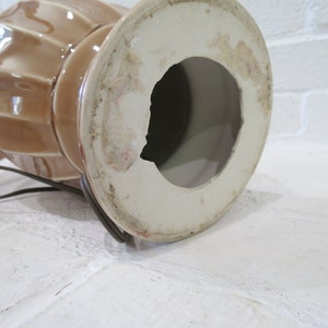 May include: The bottom of a brown ceramic lamp base with a white interior. The base has a hole in the center for the lamp cord.