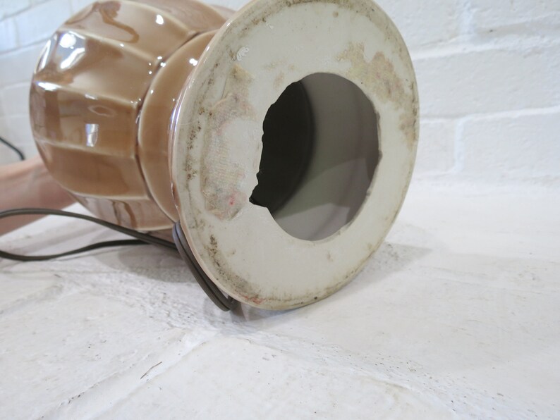 May include: The bottom of a brown ceramic lamp base with a white interior. The base has a hole in the center for the lamp cord.